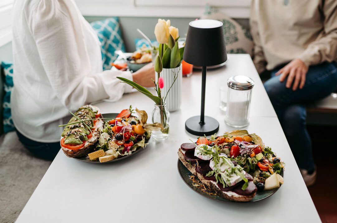 Zwei Teller mit frischem Salat und belegtem Brot auf einem Tisch in einem Café.